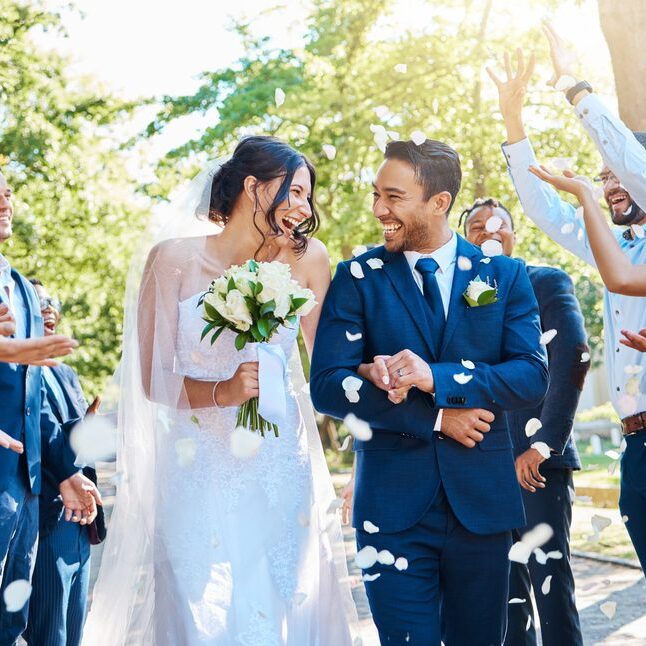 Happy, wedding ceremony and couple walking with petals and guests throw in celebration of romance. Romantic, flowers and bride with bouquet and groom with crowd celebrating at outdoor marriage event.