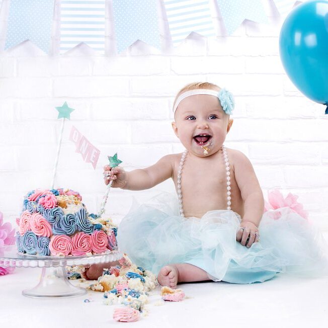 year-old girl in a blue skirt with a bandage on his head sits near a cream cake pink and blue